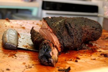 Barbecue beef brisket being shredded on a wooden cutting board.